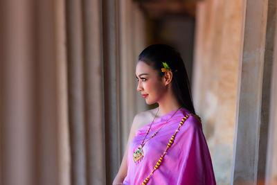 Woman looking away while standing against wall