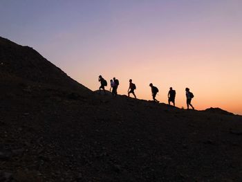 Group of people on the mountain during evening walk against sky during sunset