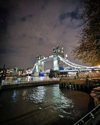 Illuminated bridge over river against sky in city at night