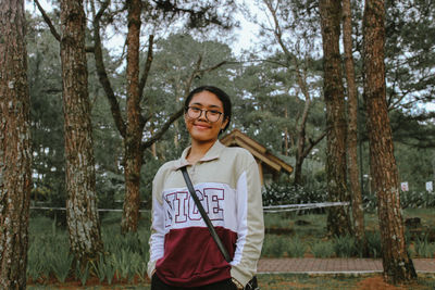 Portrait of smiling young woman standing against trees