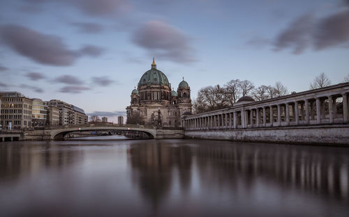 Bridge over river in city against cloudy sky