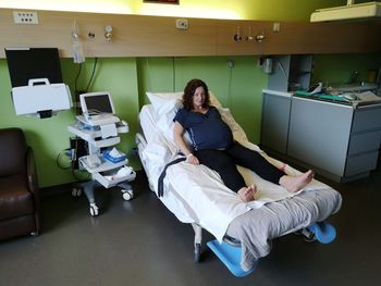 Full length portrait of pregnant woman sitting on bed at hospital