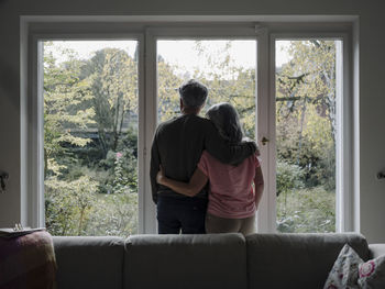 Rear view of senior couple looking out of window at home