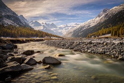 Scenic view of stream by snowcapped mountains against sky