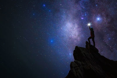 Silhouette man with flashlight standing against star field on rock