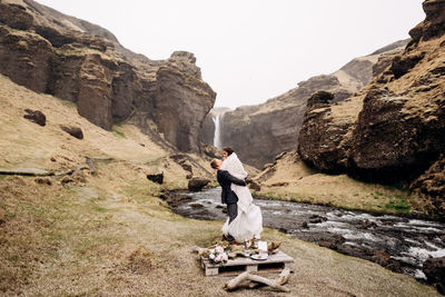 Man standing on rock by mountain against clear sky