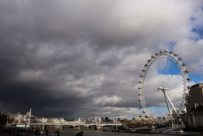 Ferris wheel in city against cloudy sky