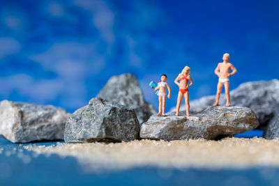 Miniature people wearing swimsuit relaxing on the beach with blue background , summer time concept