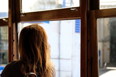 Rear view of woman looking through window at home