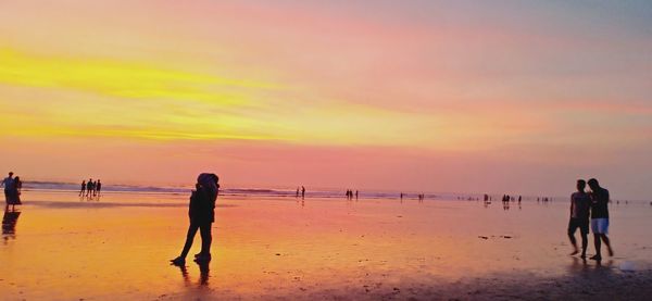 Silhouette people on beach against sky during sunset