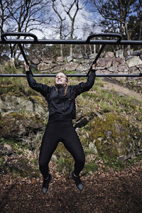 Full length of determined woman exercising on monkey bars at outdoor gym