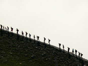 People hiking on mountain against clear sky