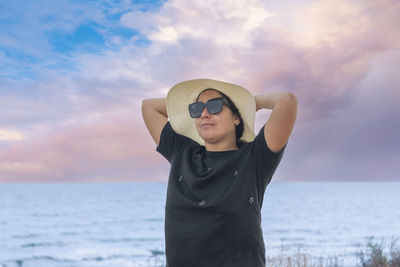 Side view of woman standing at beach against sky during sunset