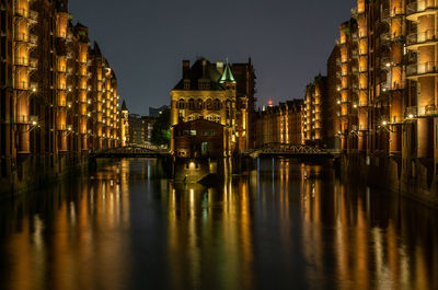 Illuminated wasserschloss buildings by river against sky at night