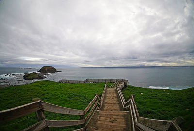 Narrow wooden jetty leading to calm sea against clouds