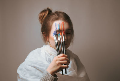 Young woman applying paint on face against wall