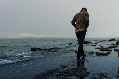 Man makes trail walking across bayside with city silhouette on horizon