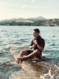 Man sitting on rock at beach against sky