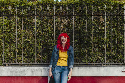 Happy woman with red hair standing in front of fence