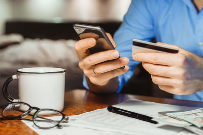 Midsection of man holding smart phone on table