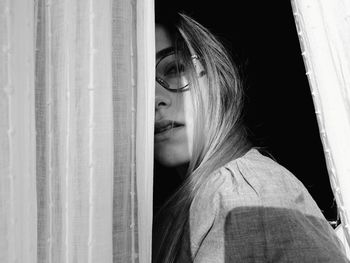 Close-up portrait of woman standing by curtain