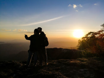 Rear view of couple standing against sky during sunset