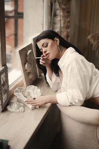 Young woman smoking cigarette by window