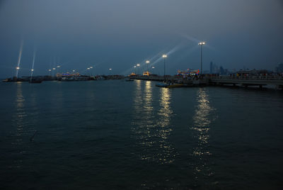 Illuminated city by sea against sky at night