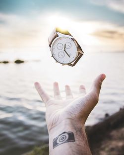 Close-up of hand holding wristwatch against sea and sky