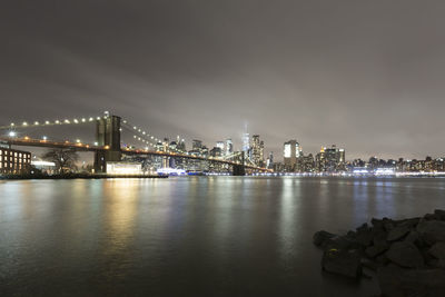 Illuminated bridge over river with buildings in background at night