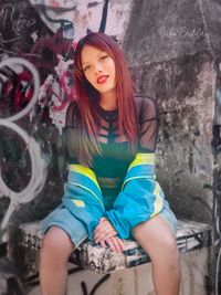 Portrait of a young woman sitting against wall