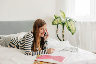 Young woman using mobile phone while sitting on bed at home