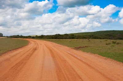 Dirt road amidst field against sky