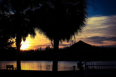 Silhouette trees by lake against sky during sunset