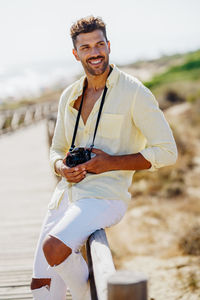 Smiling man with camera looking away while standing by railing