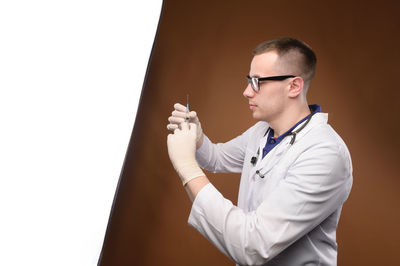 Portrait of young male doctor drawing covid-19 vaccine from vaccine bottle, with syringe and