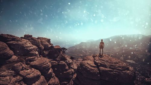 Rear view of shirtless man standing on rock against sky