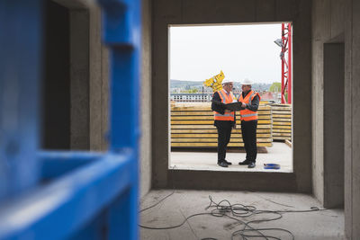 Two men wearing safety vests talking in building under construction
