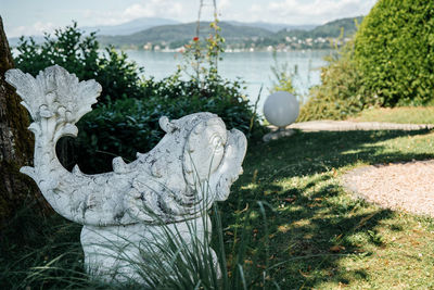 Inspired fish sculpture in garden by lakeside, surrounded by green foliage and grass