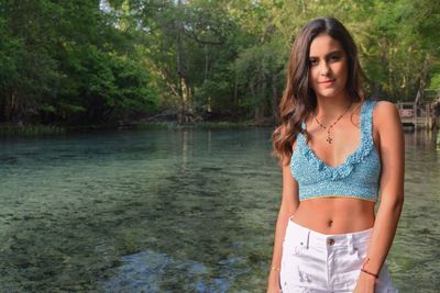 Portrait of beautiful young woman standing against lake