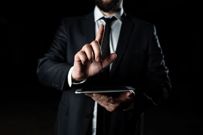 Midsection of businessman wearing suit standing against black background