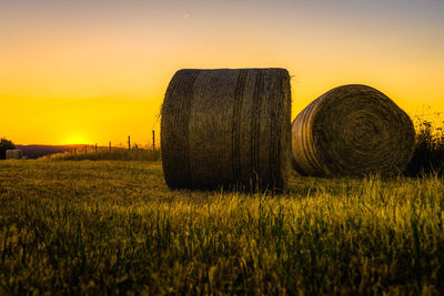 Hay bales on field against sky during sunset