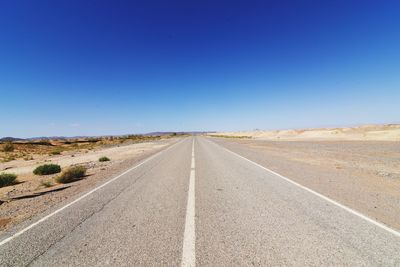 Road leading towards desert against clear sky