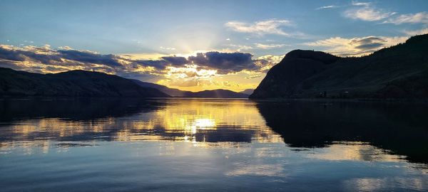 Scenic view of lake by mountains against sky during sunset