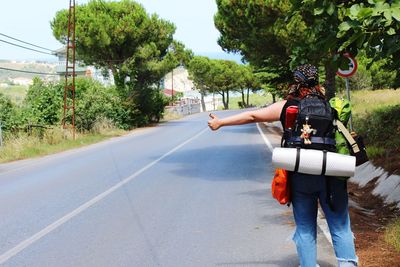 Rear view of backpack woman gesturing while standing on road