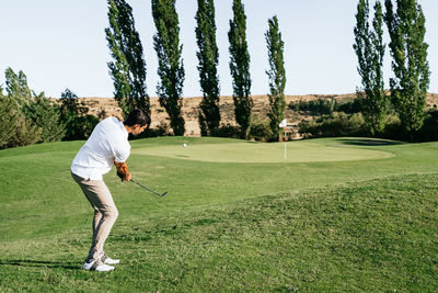 Professional male golf player preparing to hit ball with putter in green field while looking down on summer day