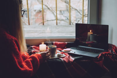 Midsection of woman looking at laptop while holding coffee