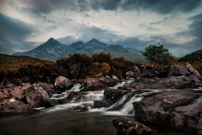 Scenic view of river flowing amidst rocks against sky