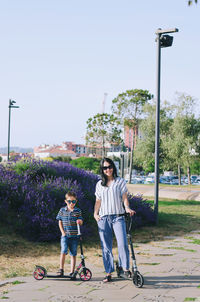 Happy family lifestyle. mother, boy, girl walking in city. ride scooters. laughing on summer. fun