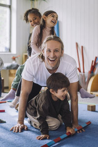 Cheerful child care worker enjoying with male and female students in kindergarten